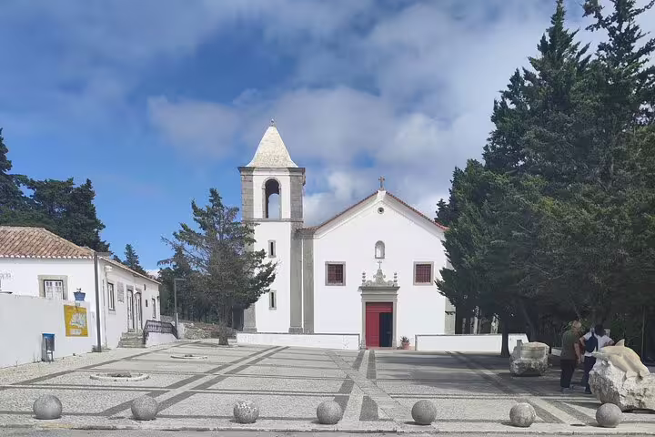 Charming white chapel among cypress trees under a blue sky in Setúbal, Portugal, highlighting cultural heritage.