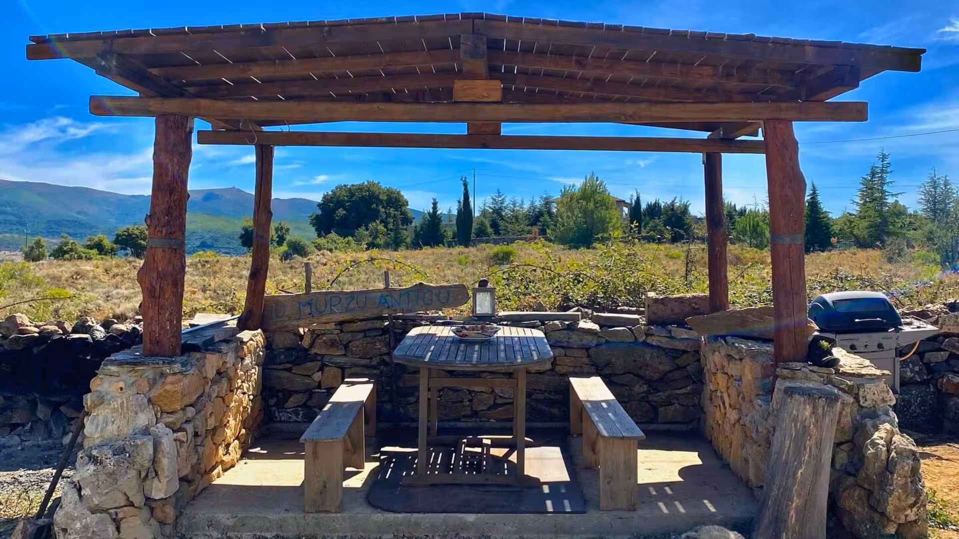 Rustic wooden pergola with a stone table and benches offers a scenic spot for tasting at Seulo farm tour in Sardinia.