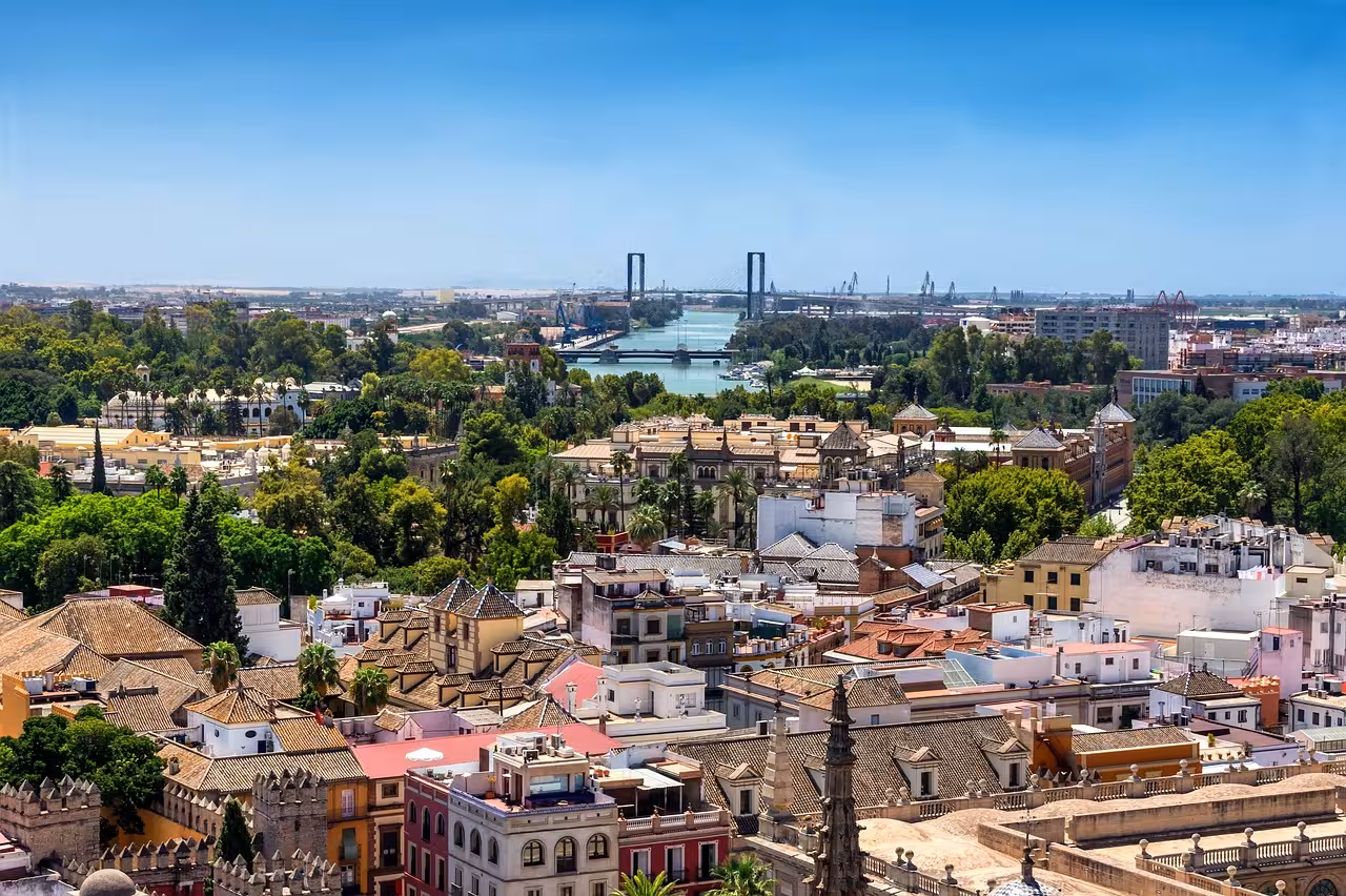 Aerial view of Seville's vibrant cityscape with lush greenery and the Guadalquivir River in the distance.