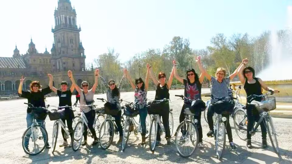 Group of cyclists enjoying Seville bike tour in front of iconic Plaza de España on a sunny day.