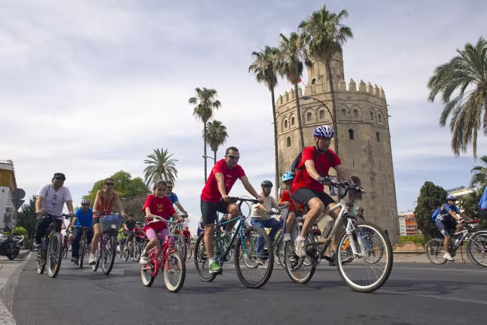 A group of cyclists passes the iconic Torre del Oro on a sunny day during a Seville city bike tour.