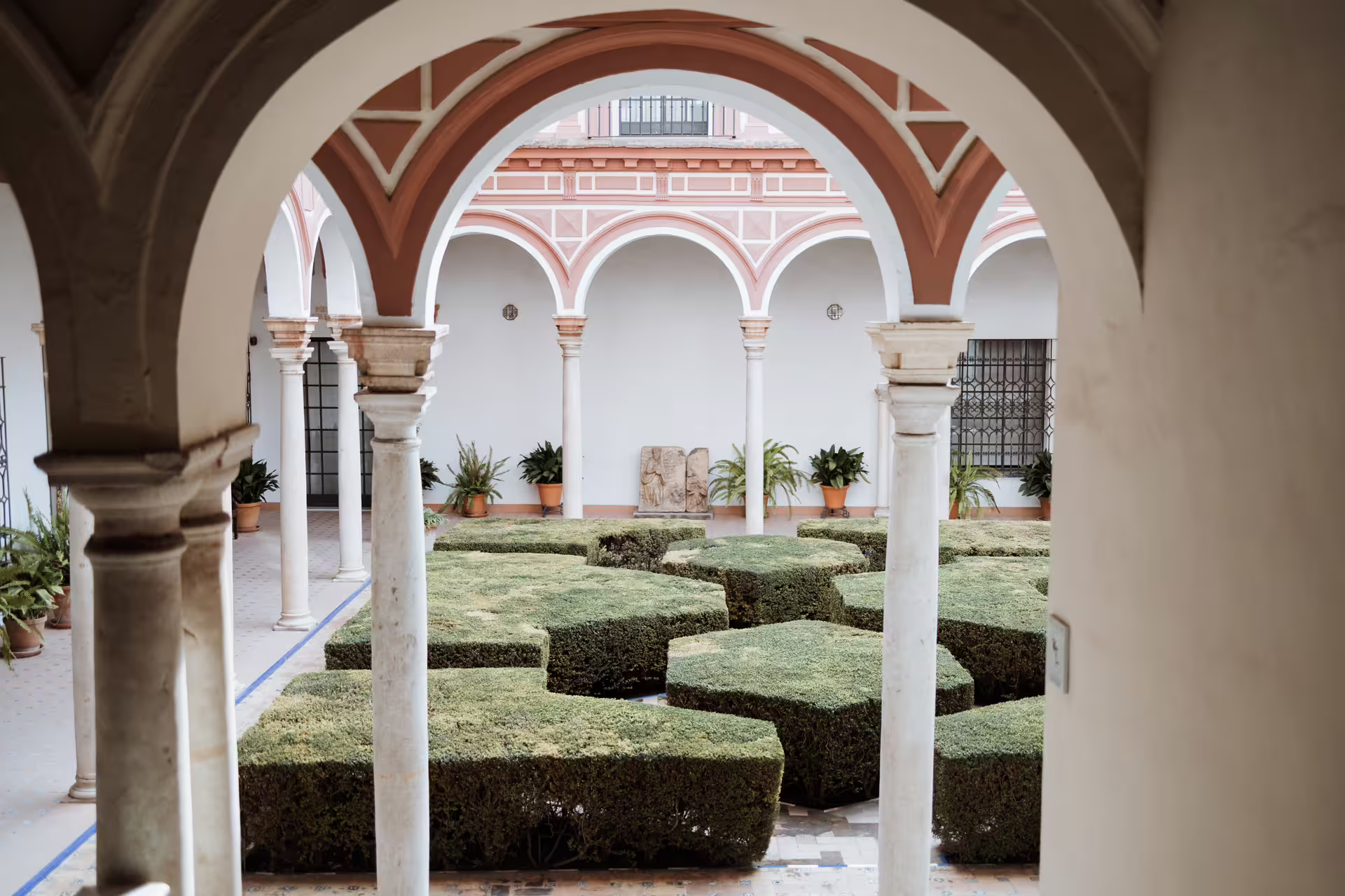 Elegant courtyard of Seville's Fine Arts Museum featuring arched columns and manicured hedges, perfect for cultural tours.