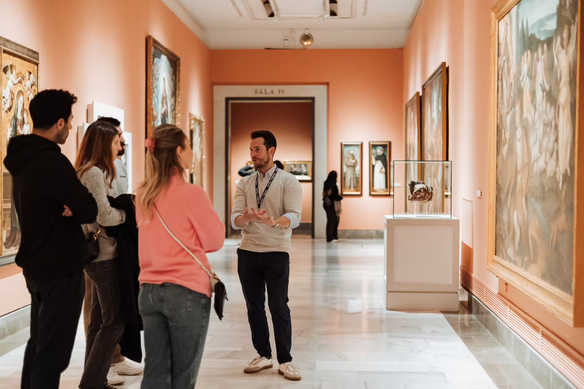 Visitors enjoy a guided tour at Seville's Fine Arts Museum, admiring classic paintings in a warmly lit gallery setting.