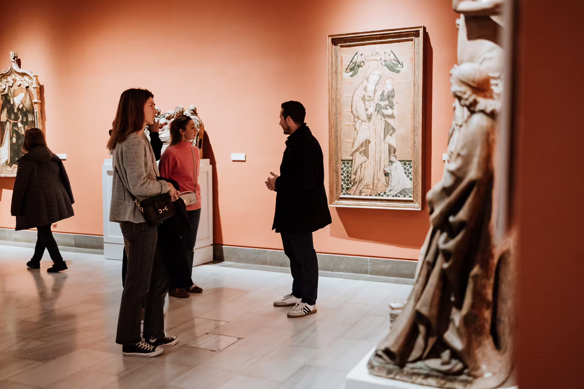 Visitors explore art exhibits during a guided tour at Seville's Fine Arts Museum, showcasing historic paintings and sculptures.