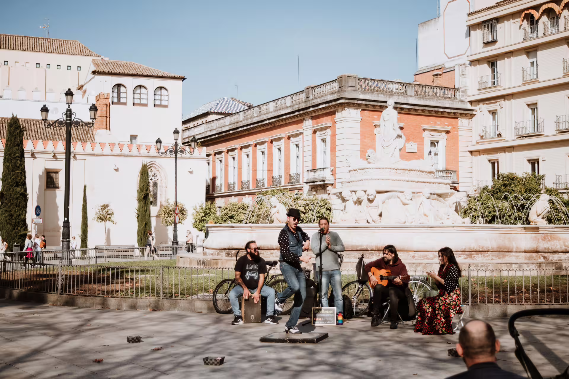 Street musicians perform lively flamenco in a sunny Seville plaza, enhancing the cultural experience of a private food tour.