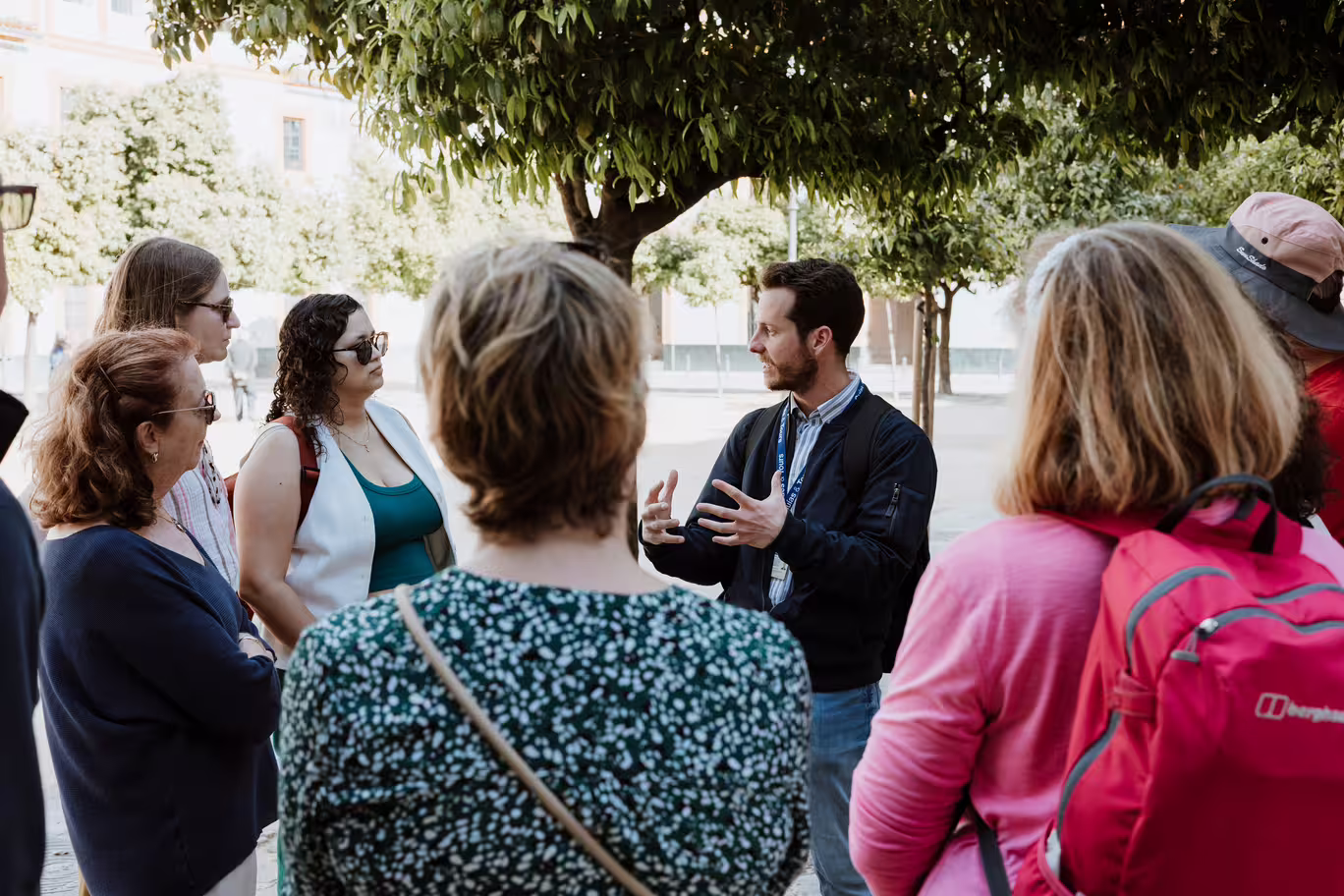 Guide leading a group tour in Seville's Santa Cruz neighborhood under a tree.