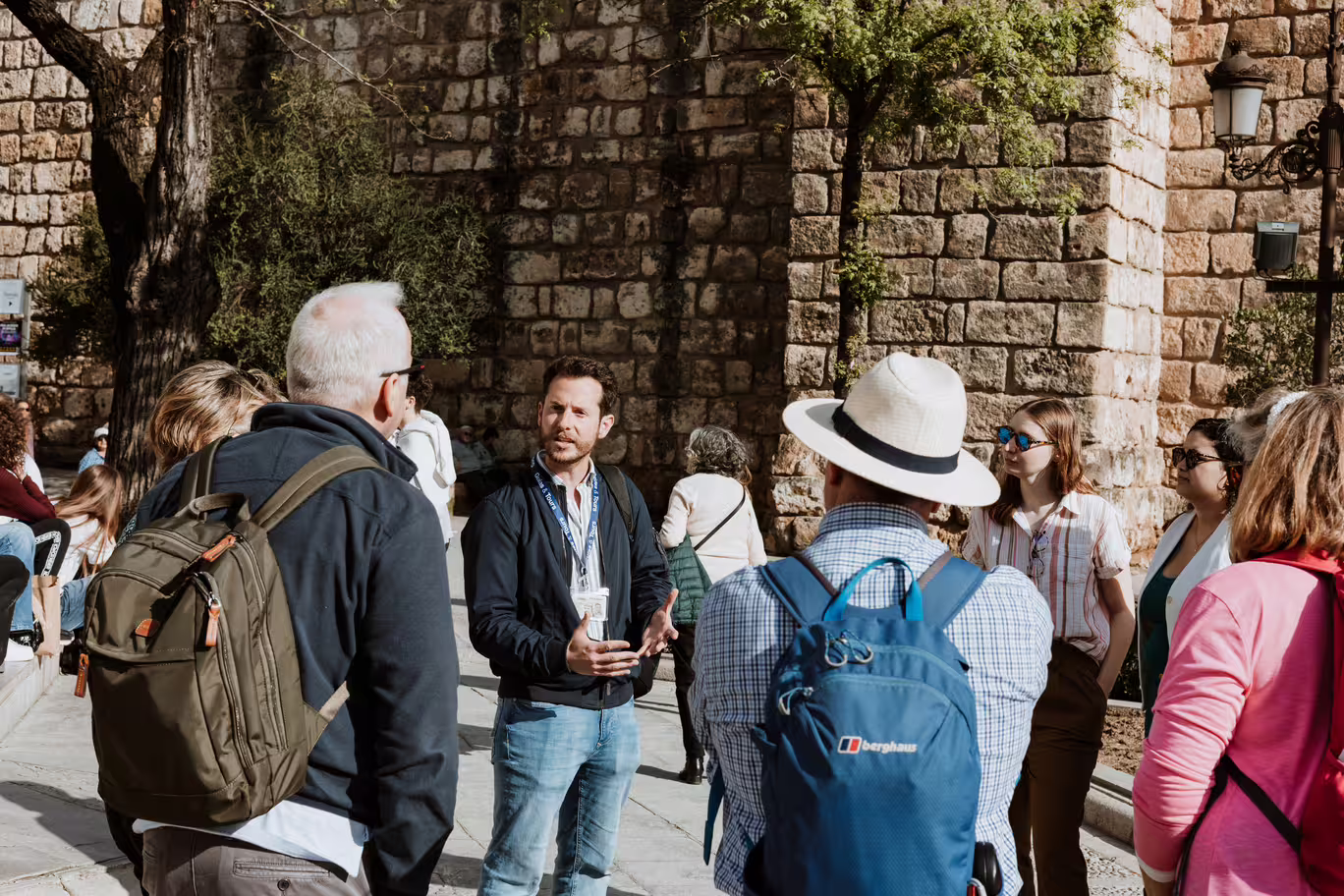 Tour guide explaining Seville's Jewish Quarter history to a group by ancient stone walls.
