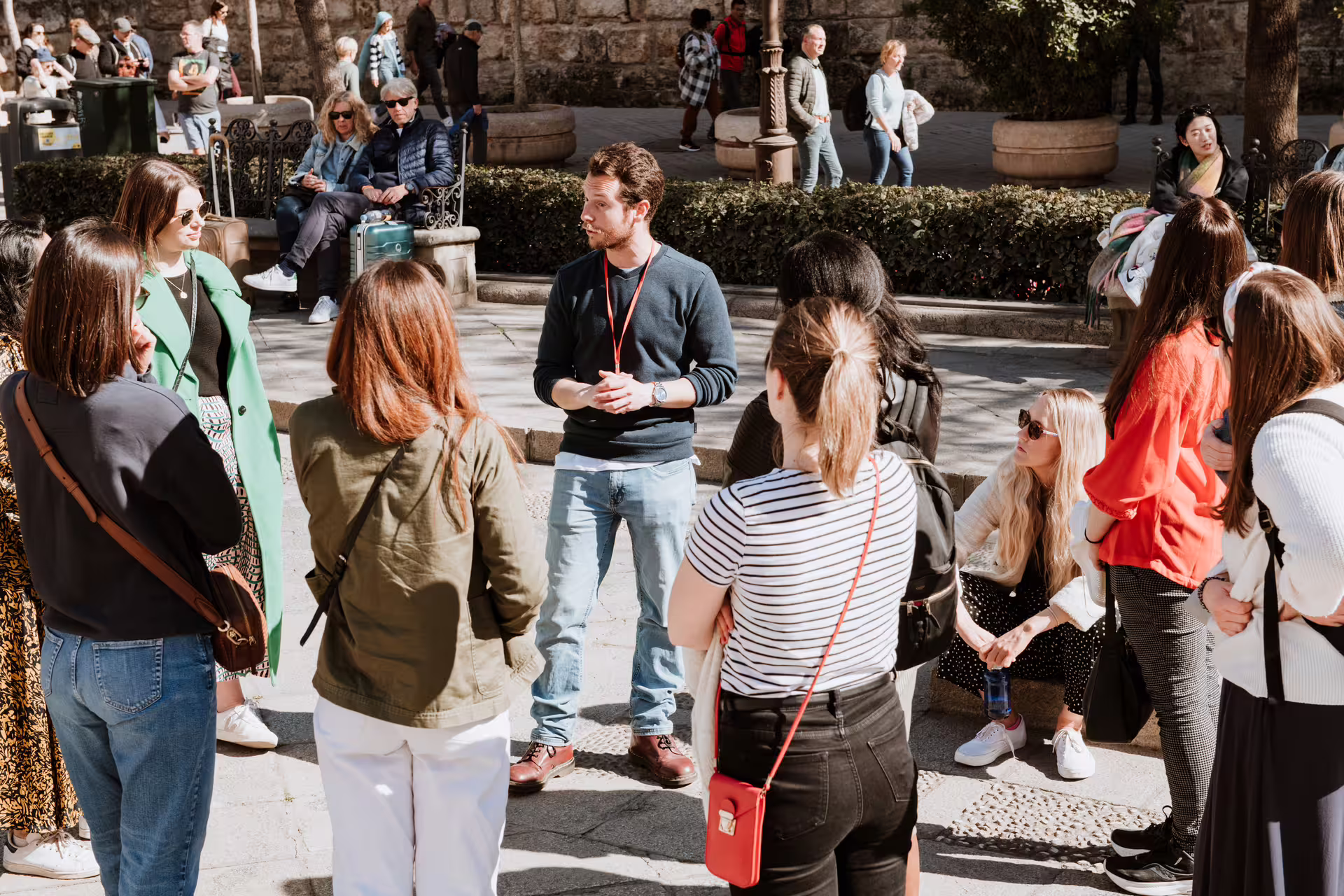 Tour group exploring Seville's Jewish Quarter with guide, enjoying sunny day in historic Santa Cruz district.