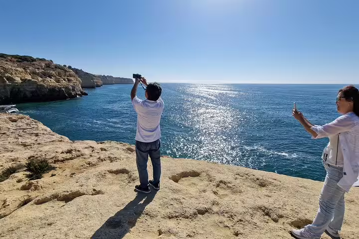 Travelers capture stunning ocean views on Algarve cliffs during a Seville to Lisbon transfer tour, highlighting scenic coastal stops.