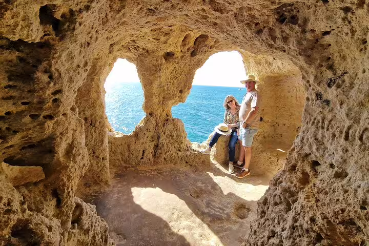Travelers enjoying scenic Algarve coastline views through rocky cave formations on a Seville to Lisbon transfer tour.