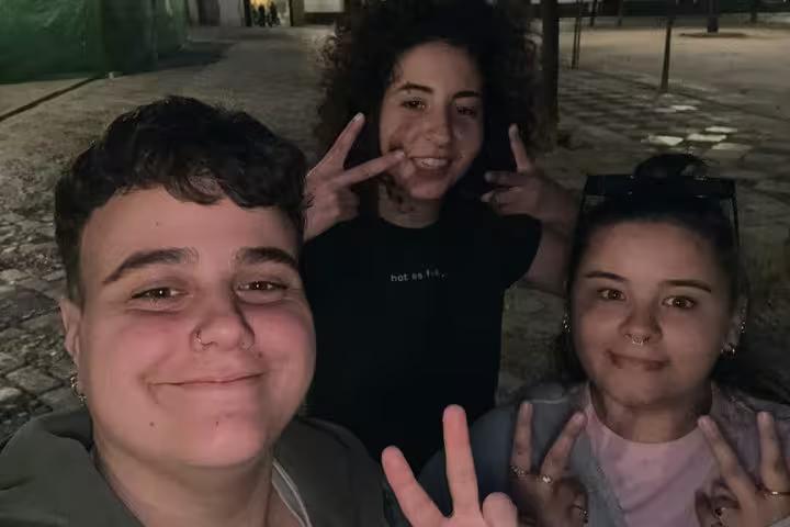 Three young friends posing with peace signs at night in Seville city streets