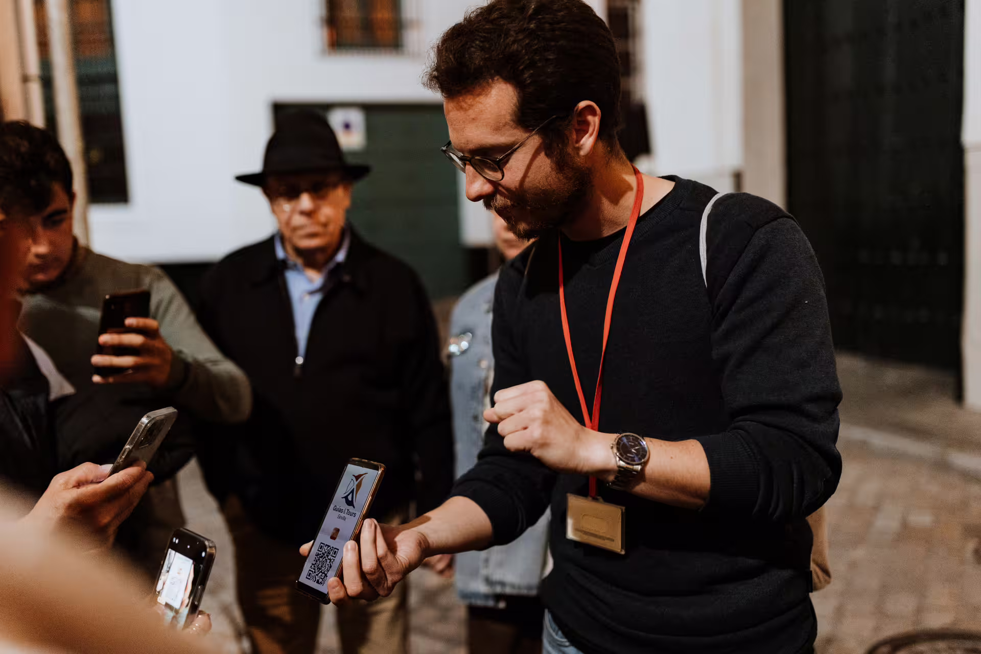 Tour guide in Seville leads a group on a mysterious and paranormal exploration, engaging with visitors using smartphones.