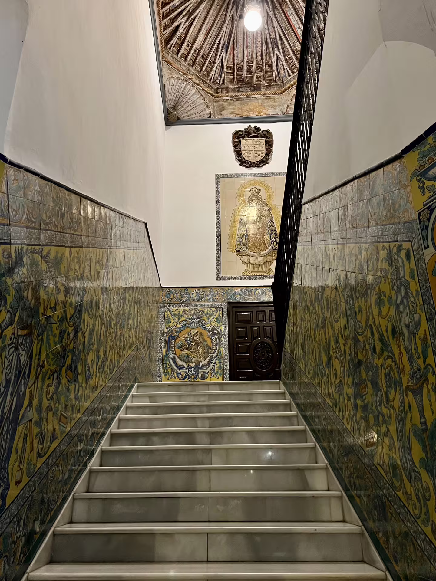Ornate staircase with intricate tiles and historic artwork in a mysterious Seville building, perfect for paranormal tours.
