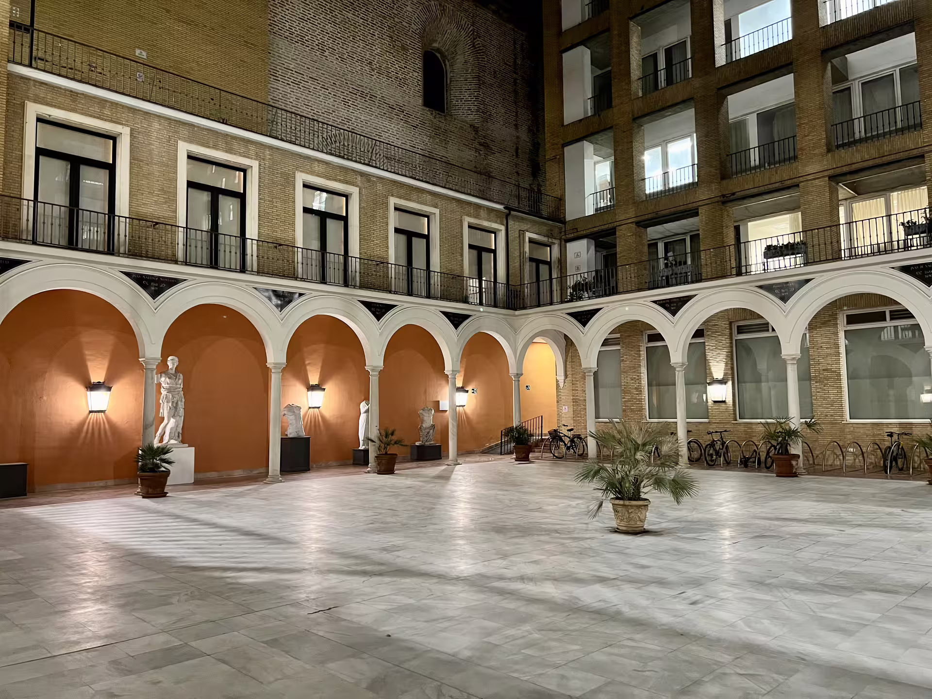 Illuminated arched courtyard in Seville at night, featuring statues and a mysterious ambiance for a paranormal tour.
