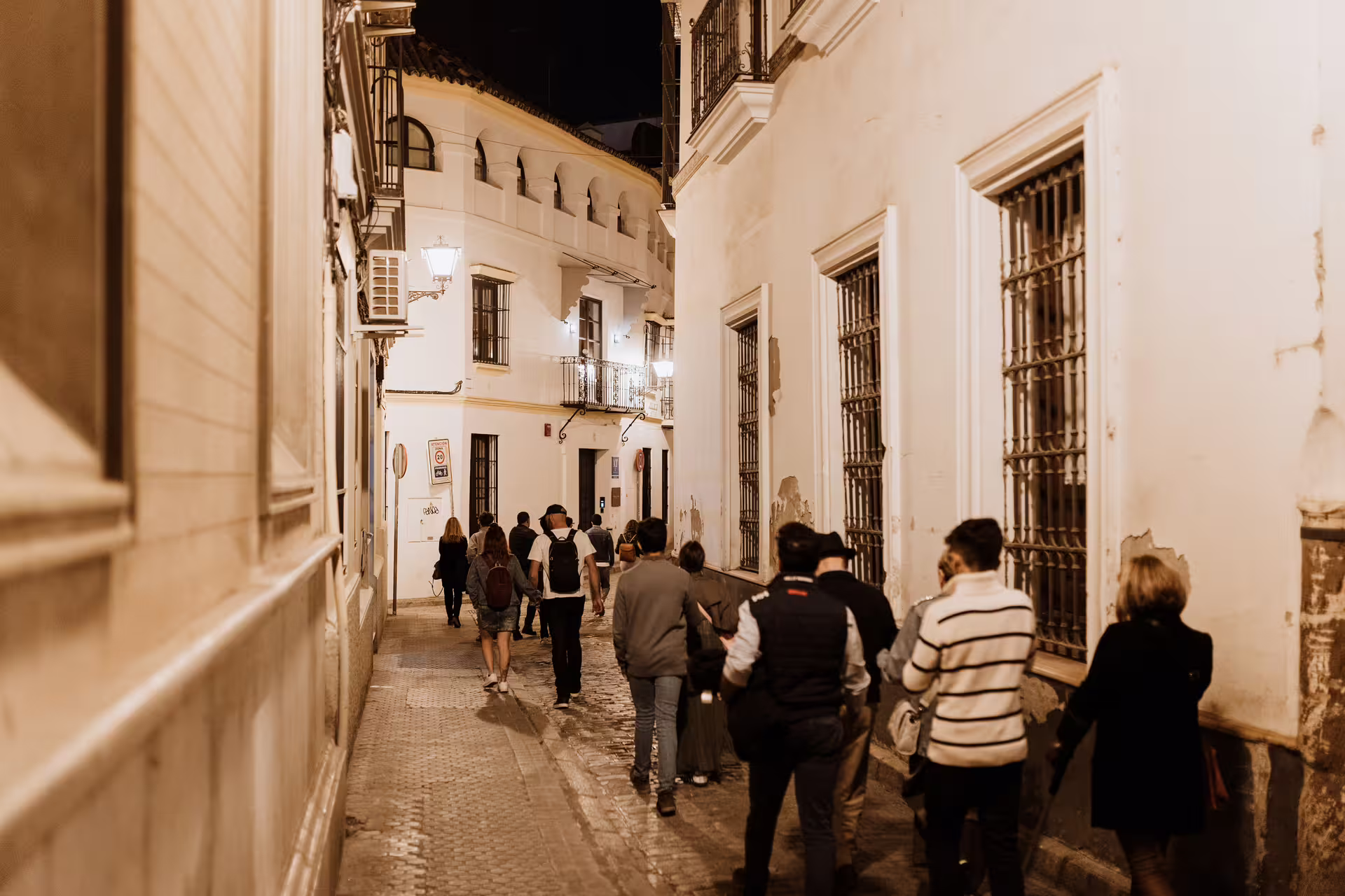 Tourists explore a narrow, dimly lit alley in Seville during a nighttime mysterious and paranormal walking tour.