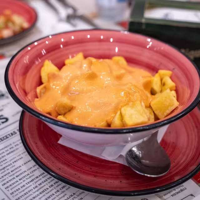 Savor traditional patatas bravas served in a vibrant red bowl on Seville's historic tapas walking tour.