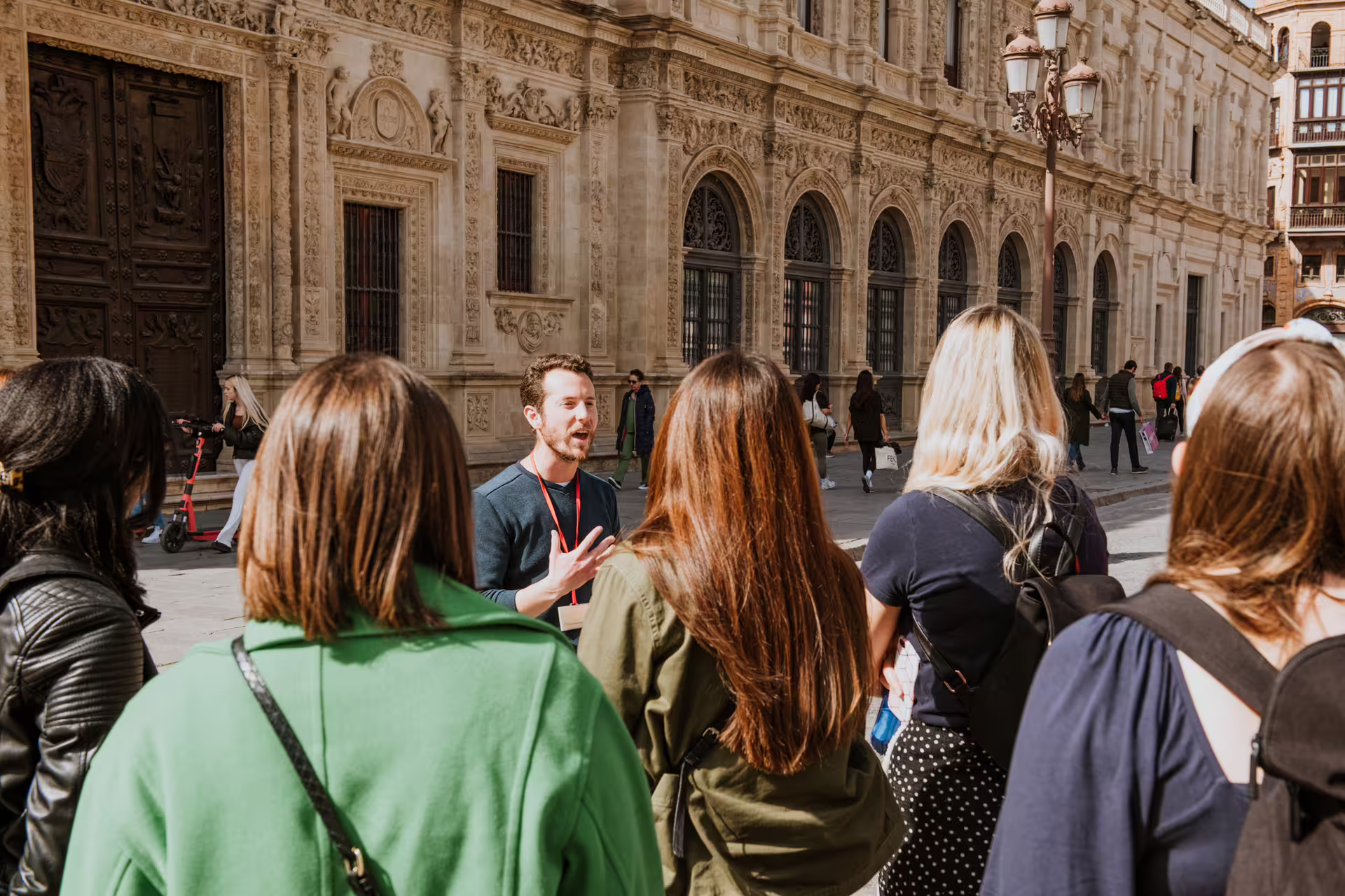 A tour guide leads a group in front of a historic building in Seville during a private food tour, under the sunny sky.