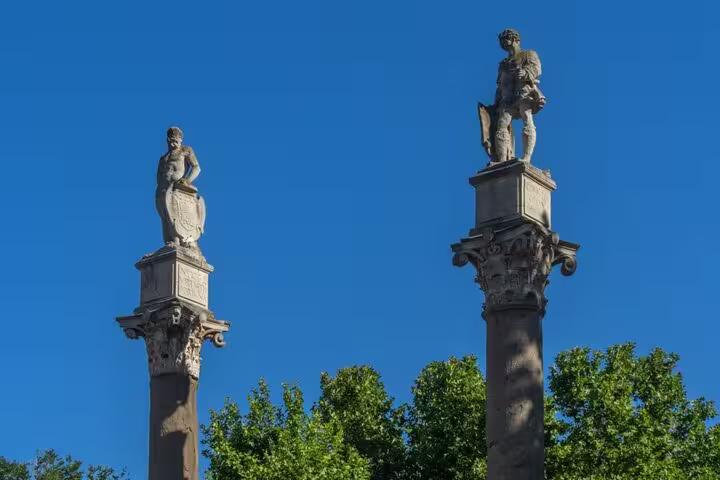 Two ancient Roman columns with statues in Seville under a clear blue sky