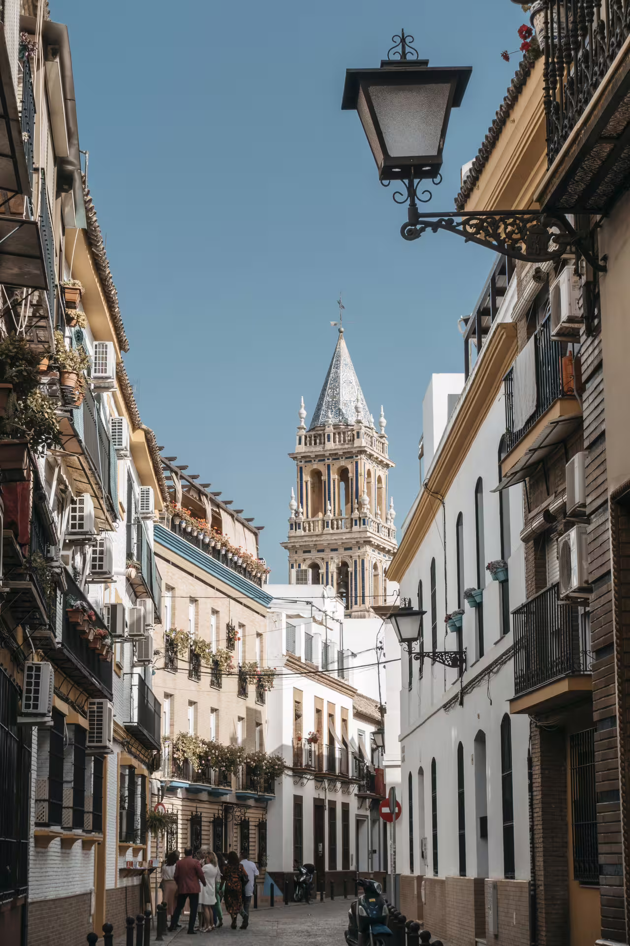 Charming narrow street in Seville's Santa Cruz neighborhood with historic architecture and iconic bell tower.