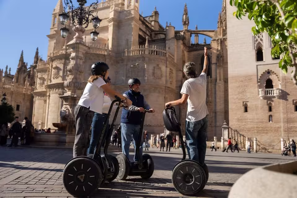 Tourists enjoy a guided Segway tour in front of Seville's historic cathedral on a sunny day.