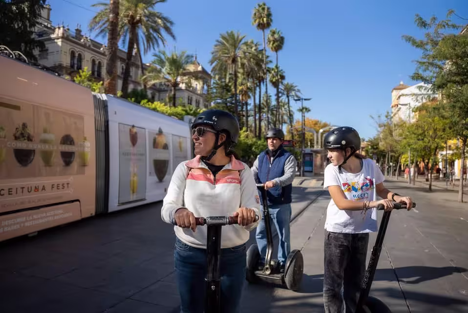 Tourists enjoying a sunny Seville city tour on Segways surrounded by historic architecture and palm trees.