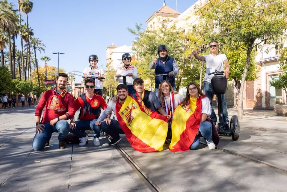 Group photo of happy tourists on a Seville Segway tour, holding Spanish flags and enjoying a sunny day.