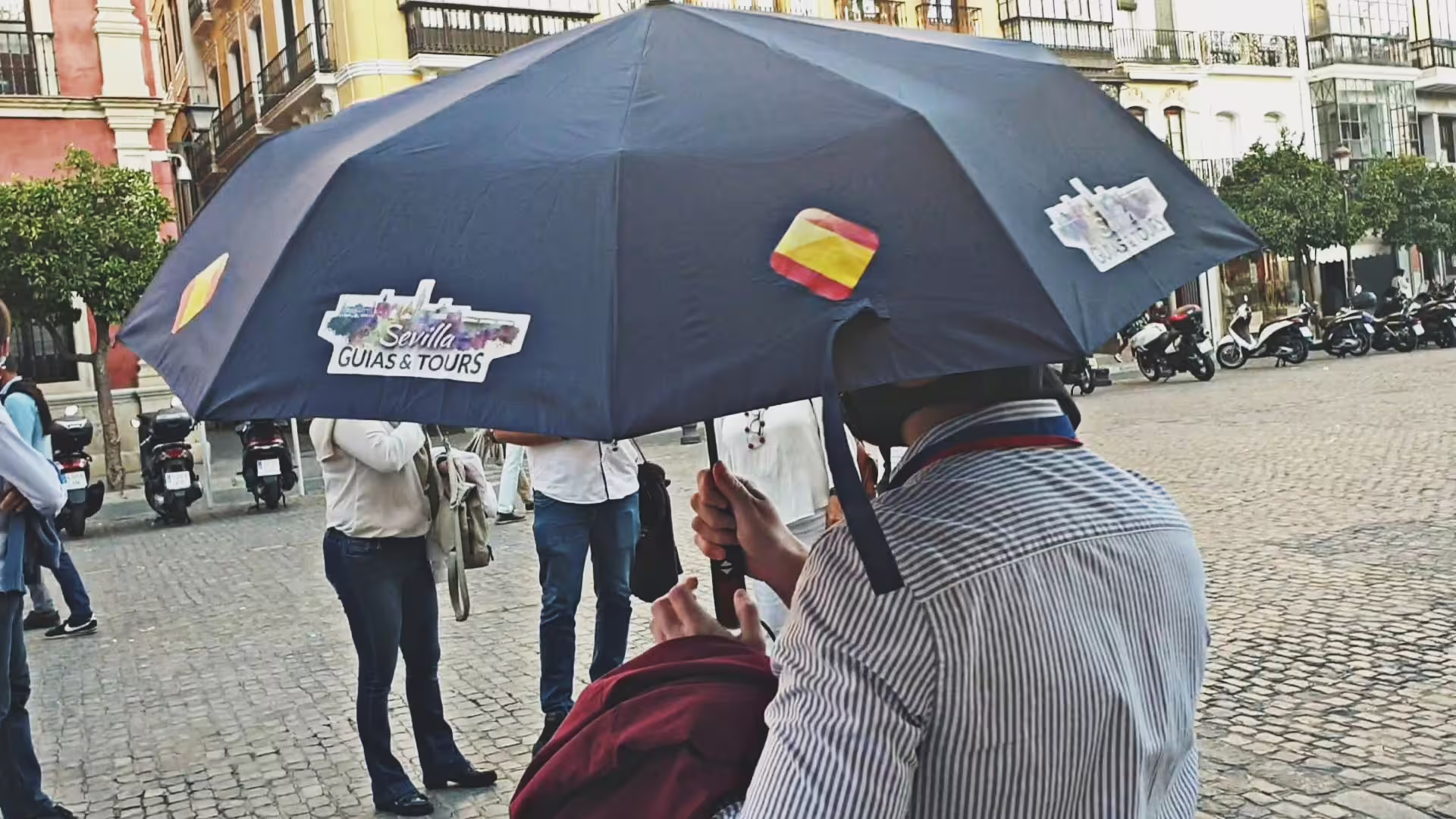 Tour guide holding a blue umbrella leading a small group through Seville's historic streets, highlighting cultural sites.