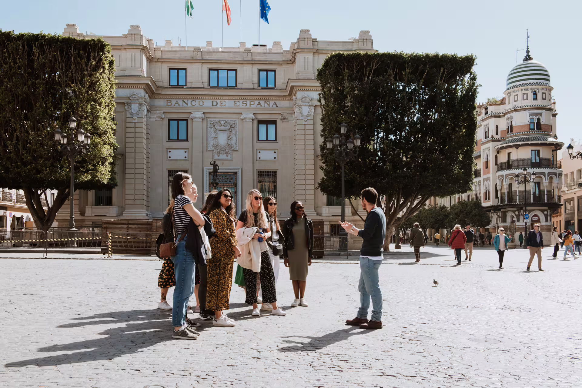 Tour guide leads a small group through Seville's historic Plaza Nueva, showcasing architectural landmarks and vibrant culture.