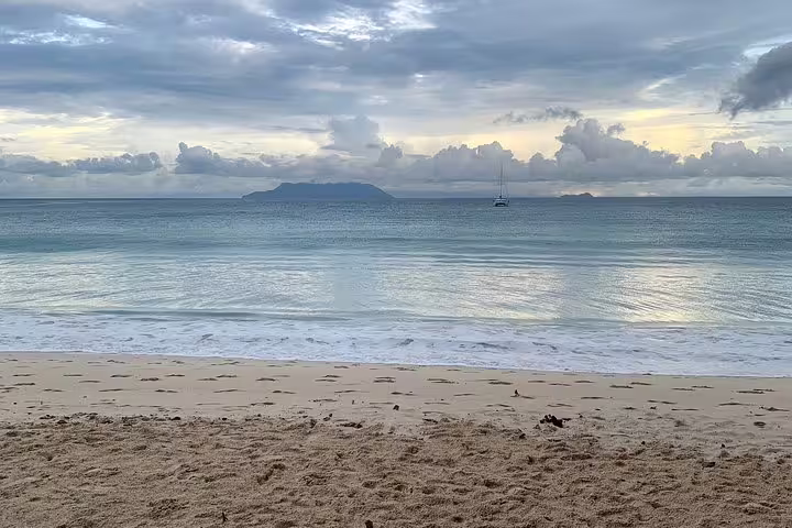 Serene Seychelles beach with gentle waves and distant island view, ideal for private island tour experience.