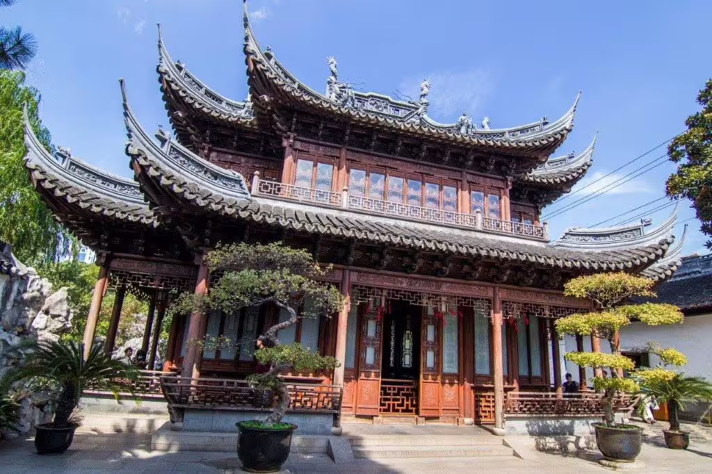 Admire the ornate wooden architecture of a historic pavilion under a clear blue sky in Shanghai's Yu Garden.