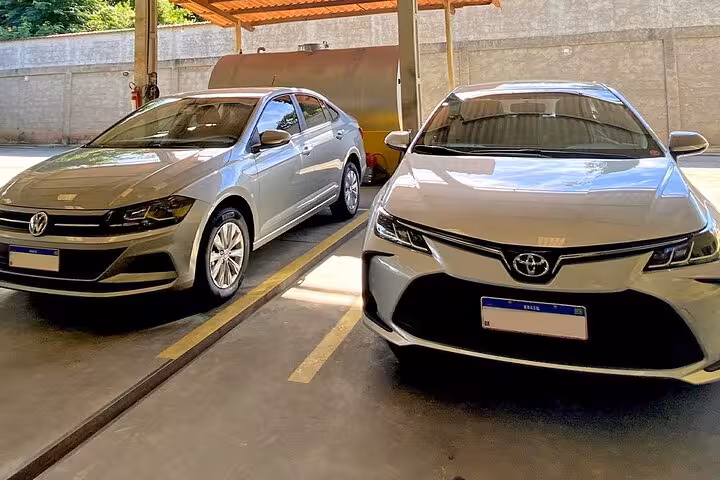 Two silver sedans parked under a covered area, ready for the shared shuttle service from Angra dos Reis to Paraty.