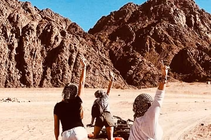 Travelers on Sharm El-Sheikh ATV desert tour pause by Sinai mountains, raising arms after quad ride