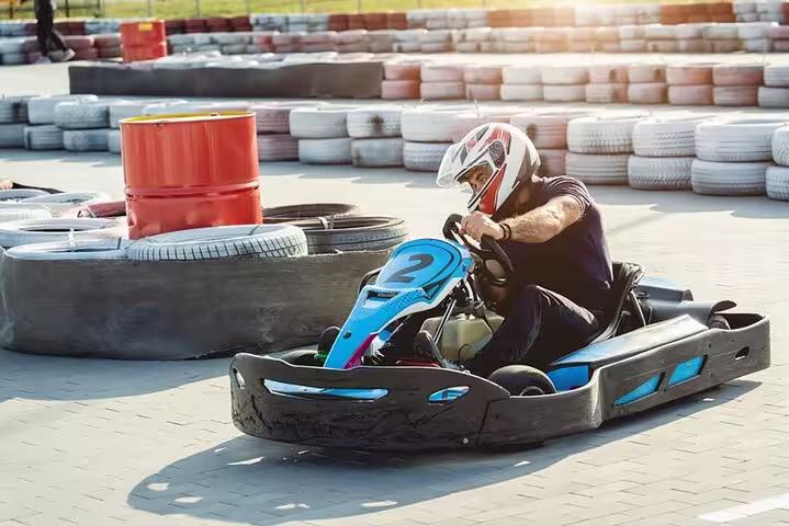Driver in helmet racing a blue go-kart on Sharm El-Sheikh Ghibli Raceway track with tire barriers