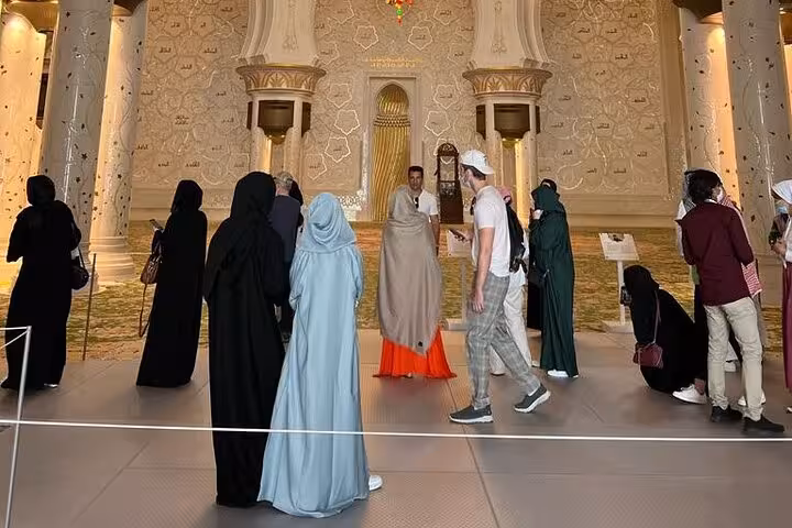 Visitors inside Sheikh Zayed Grand Mosque prayer hall on a private Abu Dhabi city tour with mosque entrance