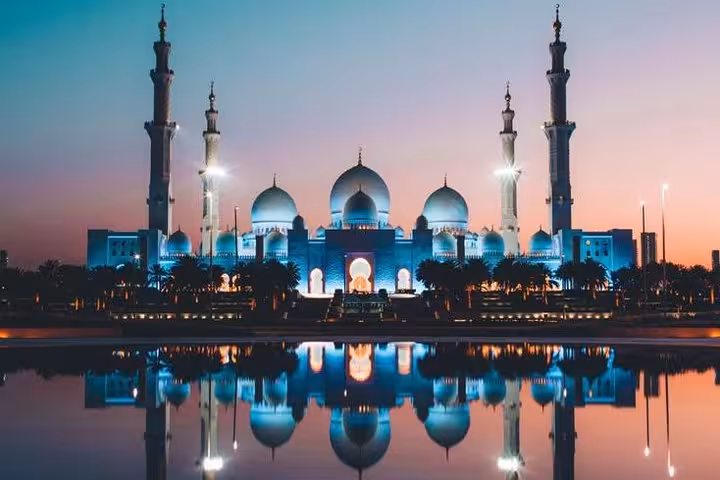 Sheikh Zayed Grand Mosque beautifully lit at twilight, mirrored in serene waters, a highlight of Abu Dhabi bus tour.