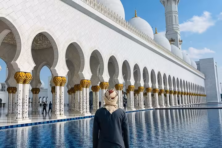 Visitor by reflecting pool at Sheikh Zayed Grand Mosque colonnade, Abu Dhabi city tour with Qasr Al Watan entry