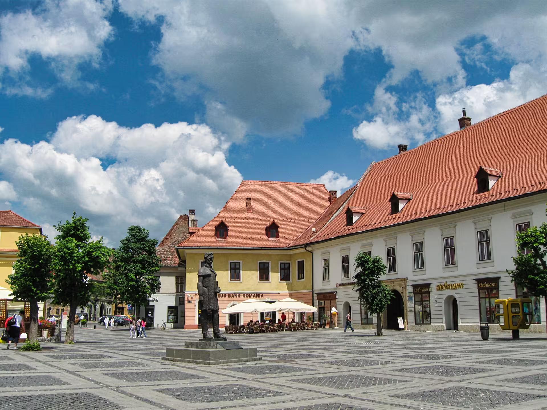 Sibiu Grand Square with bronze statue and historic Saxon buildings on a Corvin Castle day trip from Cluj-Napoca