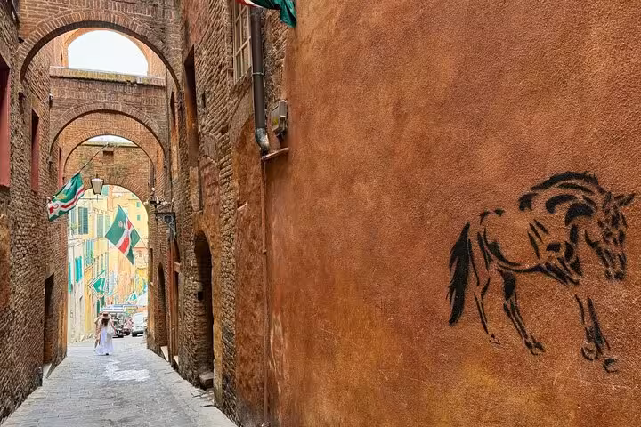 Charming alleyway in Siena with archways and horse mural, perfect for a small group tour exploring Tuscany's historic sites.