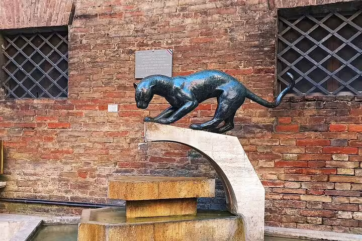 Bronze panther fountain sculpture against rustic brick wall in Siena, visited on Discover Tuscany walking tour