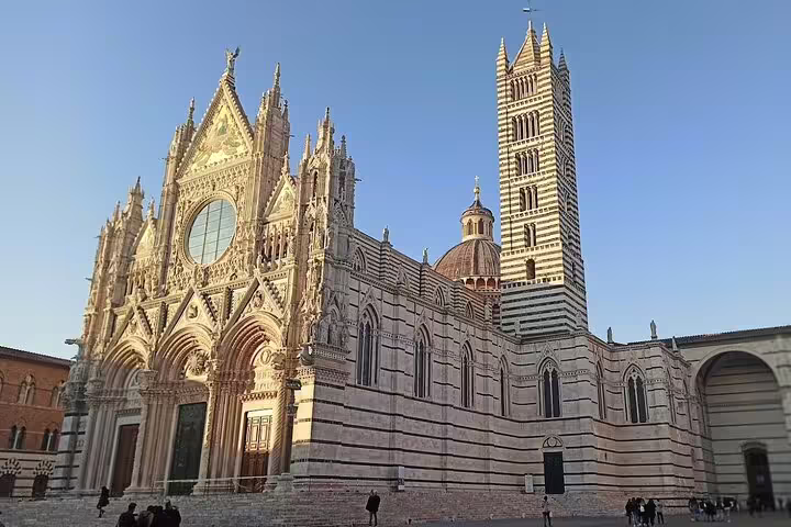 Siena Cathedral’s striped Gothic façade and bell tower glowing at sunset on a Tuscany day trip from Florence