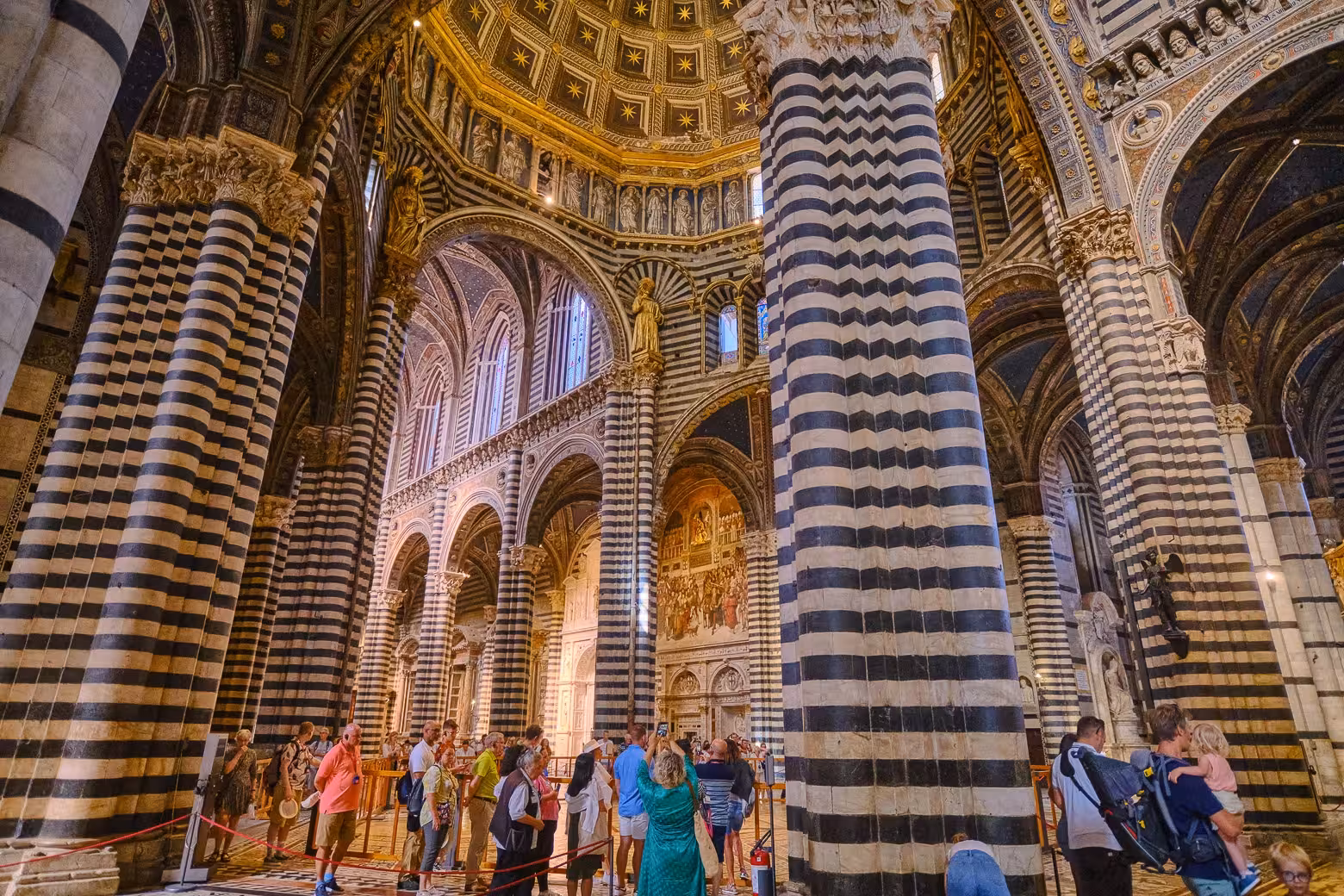 Visitors exploring the striped columns and ornate interior of Siena Cathedral on a guided Tuscany tour from Florence.
