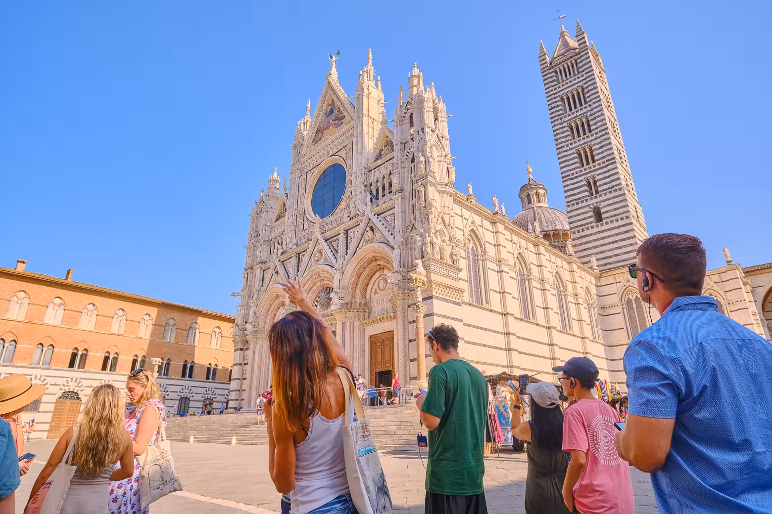 Tourists admiring the intricate facade of Siena Cathedral on a sunny day during a Tuscany highlights tour.