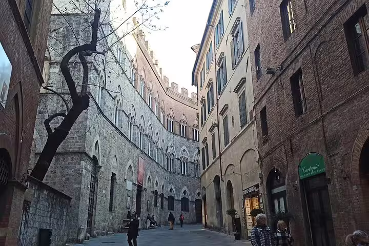 Narrow medieval alley in Siena’s historic center with stone palaces, boutiques and locals on a Tuscany walking tour