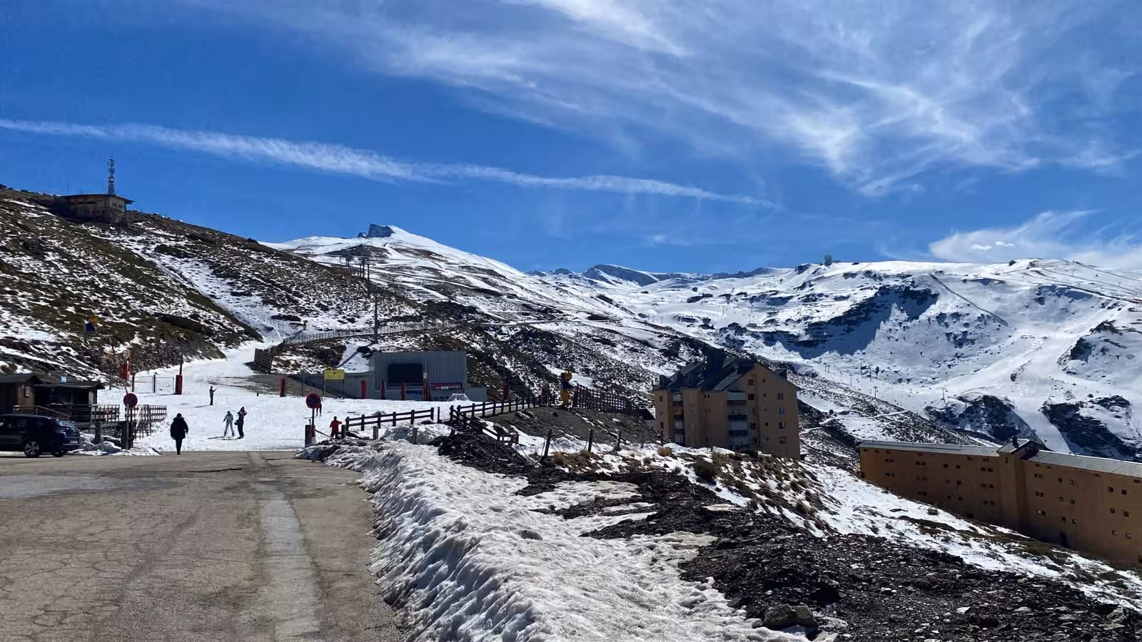 Scenic view of Sierra Nevada ski resort with snow-covered slopes and skiers under a bright blue sky.