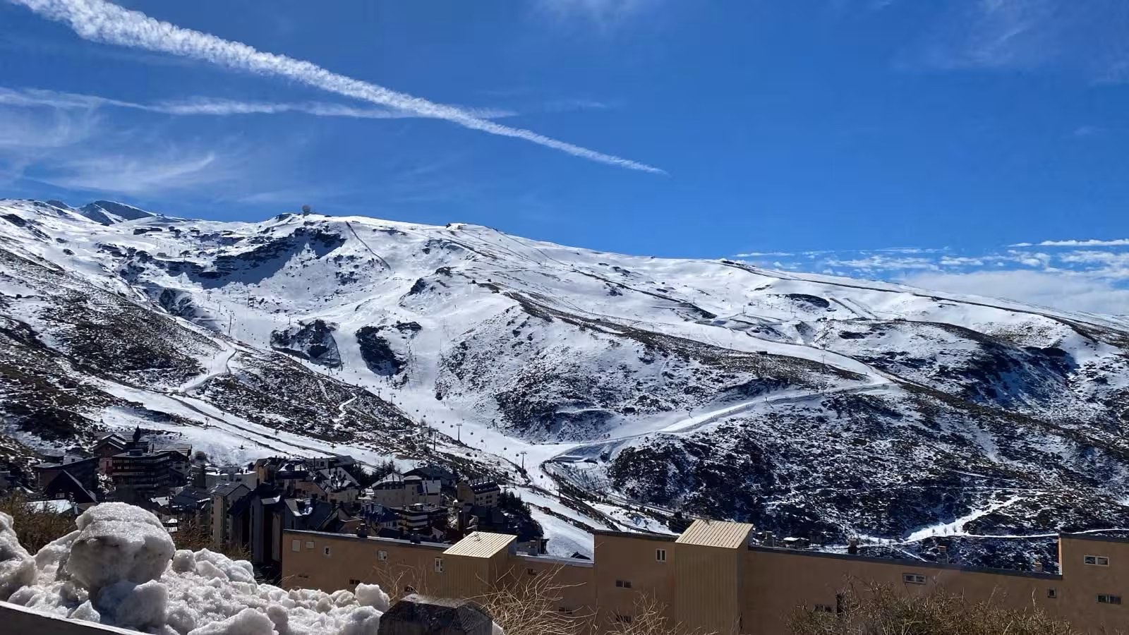 Panoramic vista of Sierra Nevada's snow-capped mountains and village nestled below under clear skies.