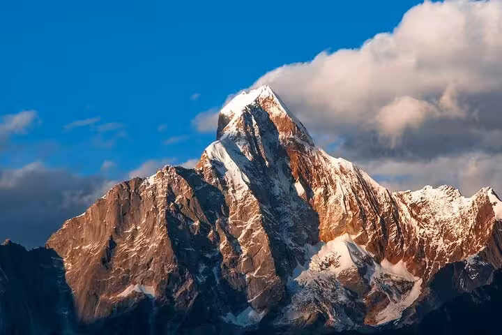 Majestic Siguniang Mountain peak bathed in sunlight, showcasing striking snow-capped cliffs against a clear blue sky.