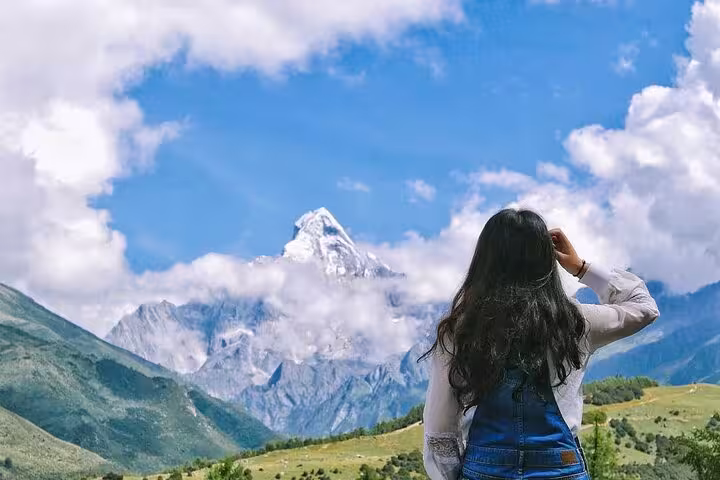 Traveler gazing at the snow-capped peak of Siguniang Mountain under a blue sky, perfect for a scenic tour adventure.