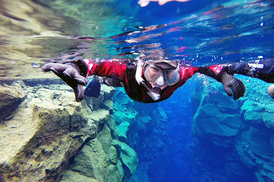 Snorkeler explores Silfra's crystal-clear waters, showcasing stunning underwater rock formations on the Cold & Hot Iceland tour.