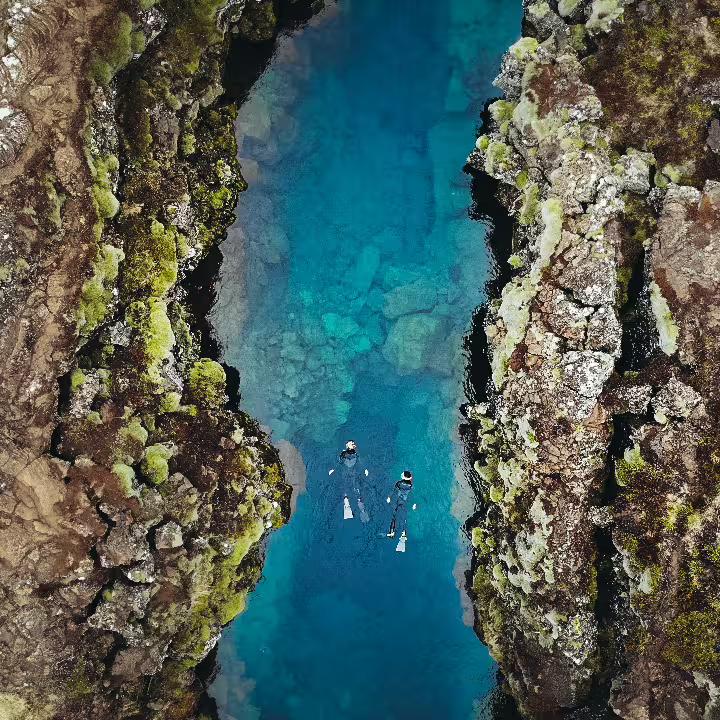 Aerial view of snorkelers exploring the crystal-clear Silfra fissure between tectonic plates in Iceland's Thingvellir National Park.