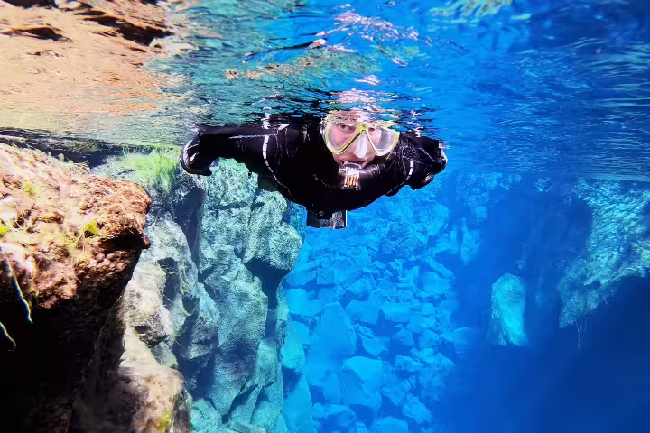 Snorkeler glides through crystal-clear waters of Silfra fissure in Iceland, showcasing vibrant underwater rock formations.